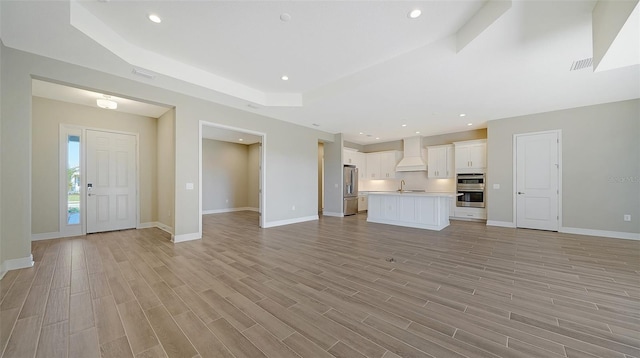 unfurnished living room with sink, light hardwood / wood-style floors, and a raised ceiling