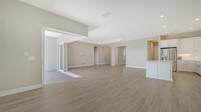 unfurnished living room featuring a raised ceiling and light wood-type flooring