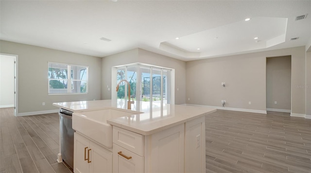 kitchen featuring white cabinets, hardwood / wood-style floors, a raised ceiling, and a center island with sink