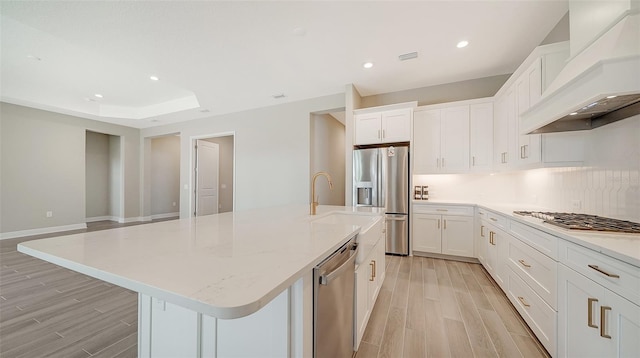 kitchen featuring light wood-type flooring, premium range hood, a kitchen island with sink, and white cabinetry