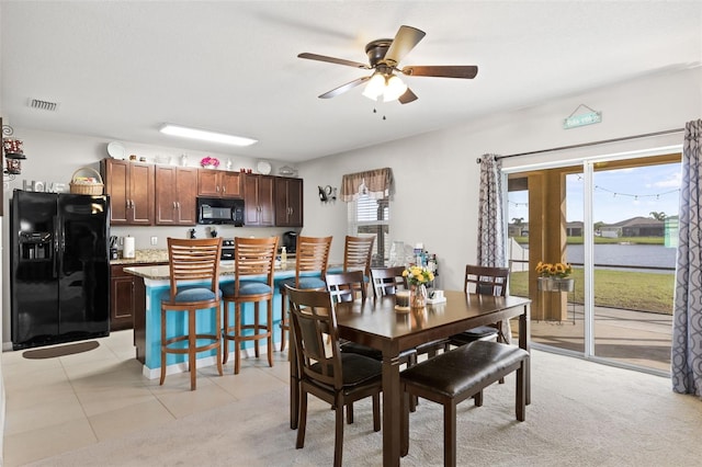 dining room featuring ceiling fan, a water view, and light tile patterned floors