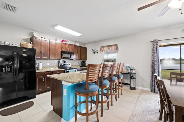 kitchen with black appliances, a kitchen island, light stone counters, a breakfast bar, and light tile patterned floors