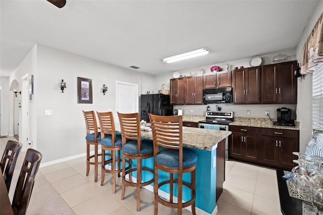 kitchen featuring light stone countertops, light tile patterned flooring, a kitchen island, black appliances, and a breakfast bar area