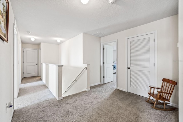 corridor with light colored carpet and a textured ceiling