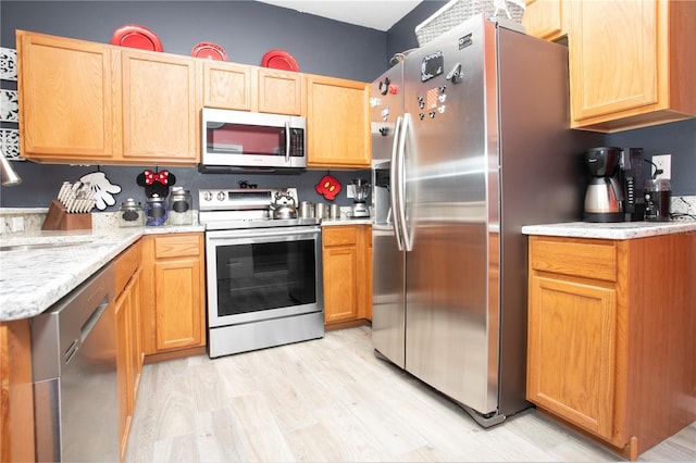 kitchen featuring sink, light hardwood / wood-style flooring, light stone countertops, and appliances with stainless steel finishes