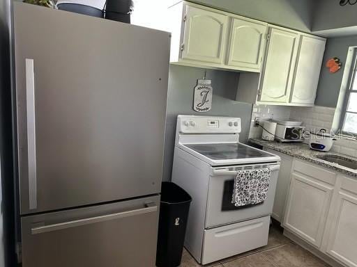 kitchen with electric stove, light tile patterned floors, decorative backsplash, freestanding refrigerator, and a sink