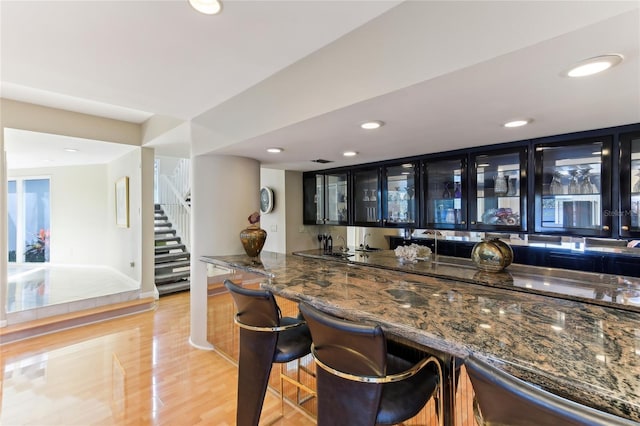 bar with light hardwood / wood-style floors and dark stone countertops