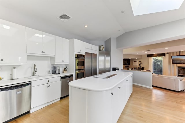 kitchen featuring lofted ceiling with skylight, a kitchen island, appliances with stainless steel finishes, white cabinets, and light hardwood / wood-style flooring