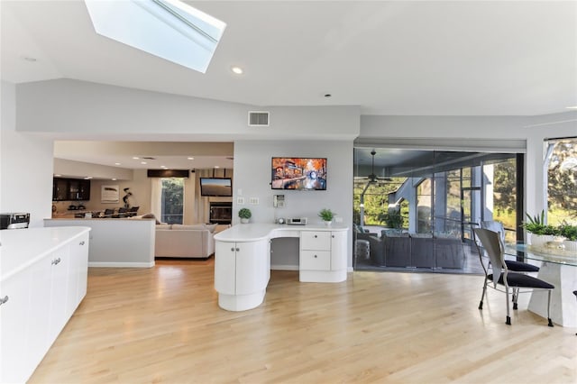 kitchen featuring white cabinetry, a center island, vaulted ceiling with skylight, and light wood-type flooring