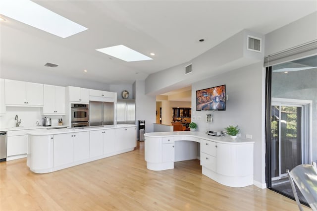 kitchen featuring appliances with stainless steel finishes, white cabinetry, light hardwood / wood-style floors, a kitchen island, and kitchen peninsula