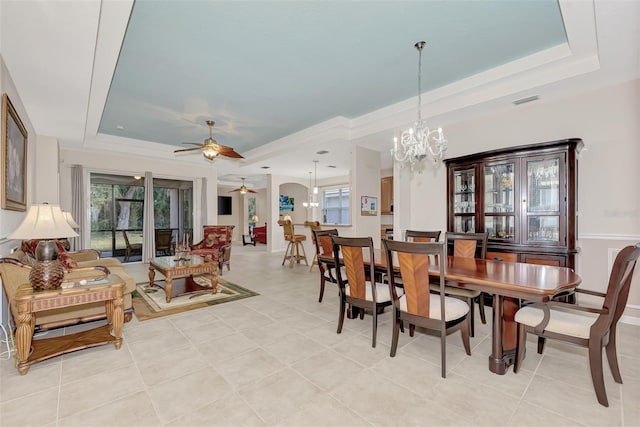 tiled dining area with ceiling fan with notable chandelier and a tray ceiling