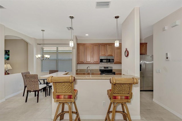 kitchen featuring an inviting chandelier, a breakfast bar, stainless steel appliances, light stone counters, and pendant lighting