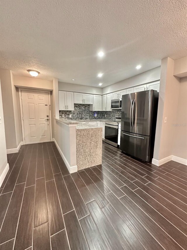 kitchen with white cabinetry, decorative backsplash, kitchen peninsula, stainless steel appliances, and light stone countertops