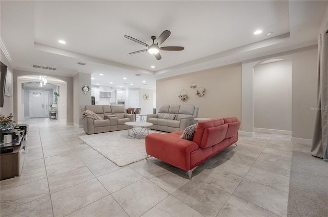 living room featuring a raised ceiling, light tile patterned flooring, ornamental molding, and ceiling fan