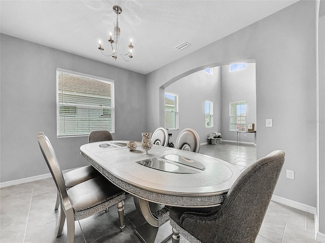 dining space with arched walkways, light tile patterned floors, a chandelier, visible vents, and baseboards