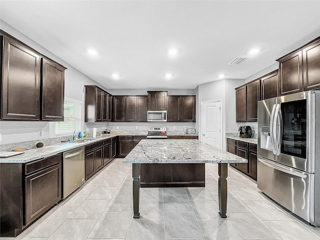 kitchen with dark brown cabinetry, stainless steel appliances, a sink, visible vents, and light stone countertops