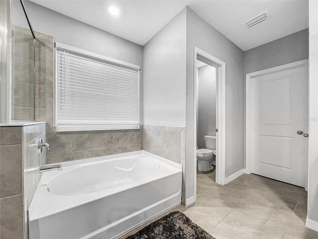 full bath featuring toilet, a garden tub, visible vents, and baseboards