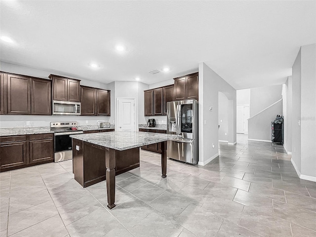 kitchen featuring a breakfast bar area, a center island, dark brown cabinets, appliances with stainless steel finishes, and light stone countertops