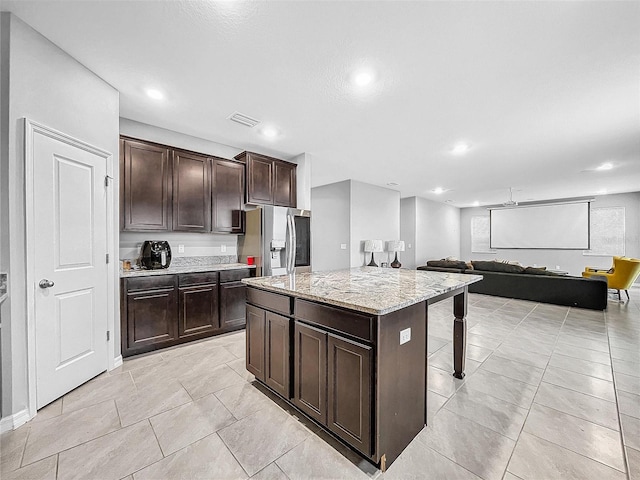 kitchen featuring visible vents, open floor plan, a kitchen island, light stone countertops, and stainless steel fridge