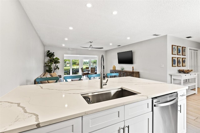 kitchen with ceiling fan, dishwasher, sink, white cabinetry, and light stone countertops