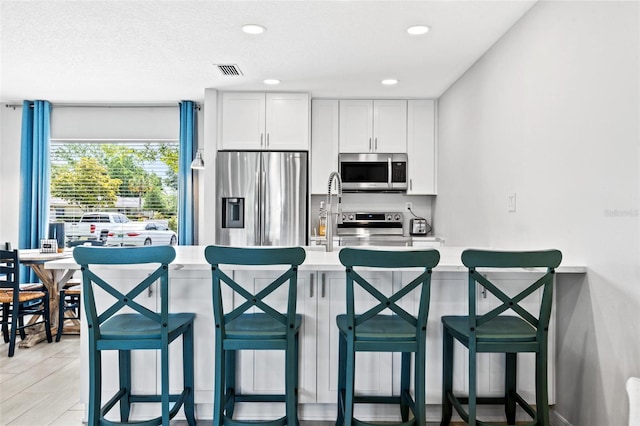 kitchen with appliances with stainless steel finishes, white cabinetry, and a breakfast bar