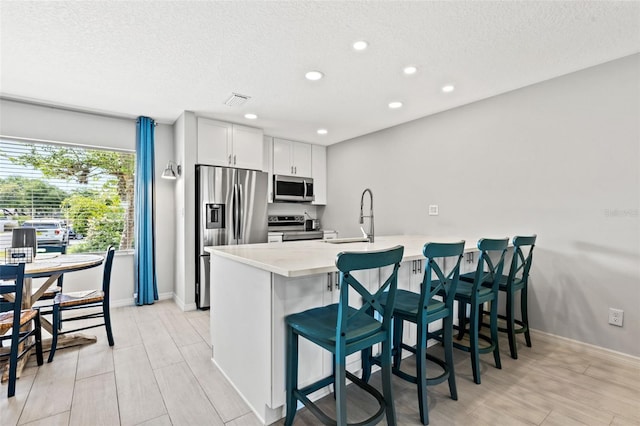 kitchen featuring kitchen peninsula, sink, appliances with stainless steel finishes, a kitchen breakfast bar, and white cabinets