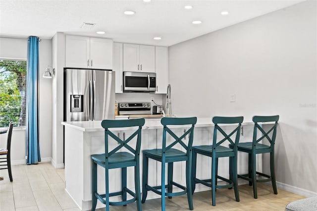 kitchen featuring kitchen peninsula, stainless steel appliances, a kitchen bar, and white cabinetry