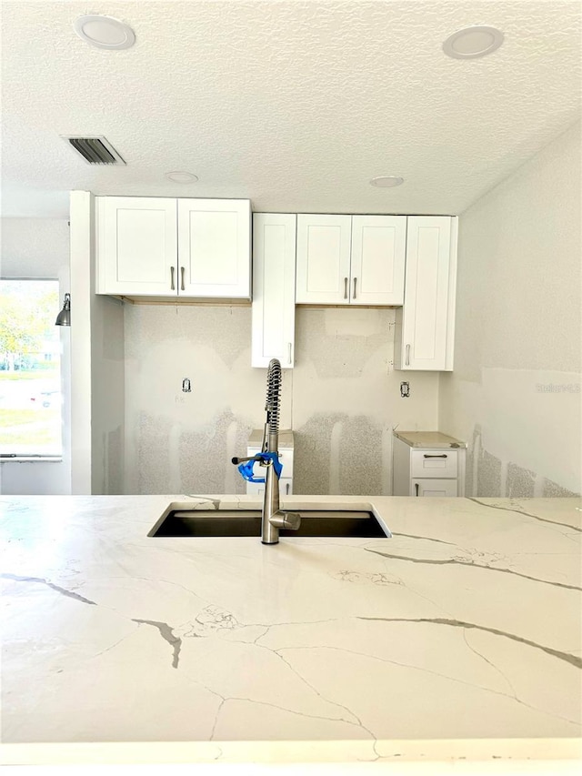 kitchen with light stone countertops, sink, and white cabinetry