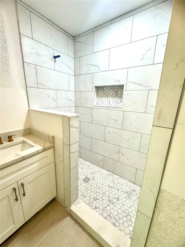 bathroom with wood-type flooring, tiled shower, and vanity