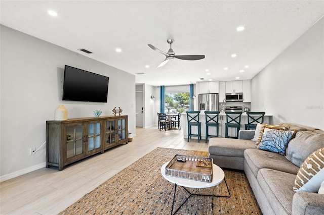 living room featuring ceiling fan, a textured ceiling, and light hardwood / wood-style flooring