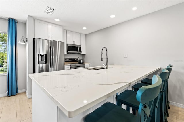 kitchen featuring a kitchen breakfast bar, appliances with stainless steel finishes, white cabinets, and sink