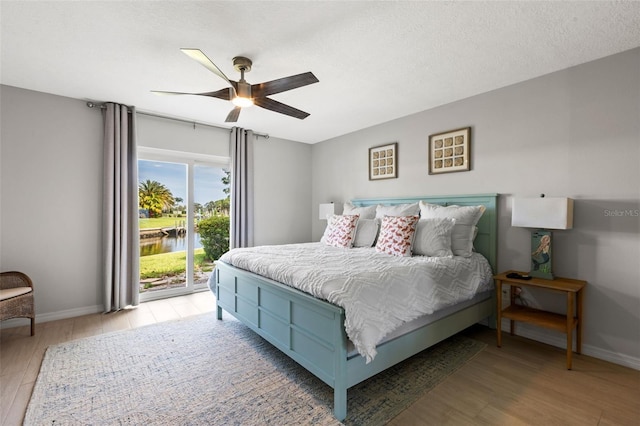 bedroom with ceiling fan, access to exterior, a water view, and light hardwood / wood-style flooring