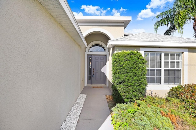 doorway to property featuring stucco siding and a shingled roof