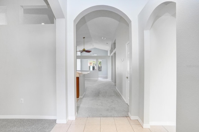 hall with lofted ceiling, light tile patterned flooring, baseboards, and light carpet