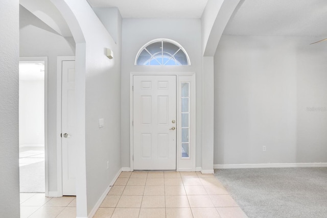 foyer with light tile patterned floors, arched walkways, and baseboards