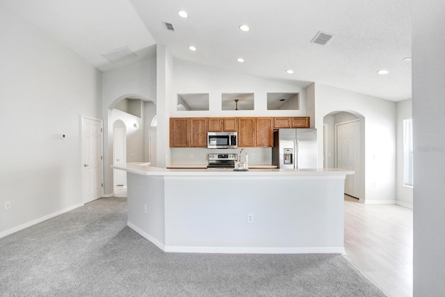 kitchen featuring a kitchen island with sink, appliances with stainless steel finishes, high vaulted ceiling, and light colored carpet