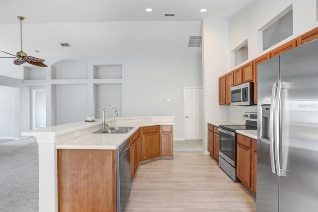 kitchen with light wood-type flooring, a high ceiling, stainless steel appliances, sink, and a center island with sink