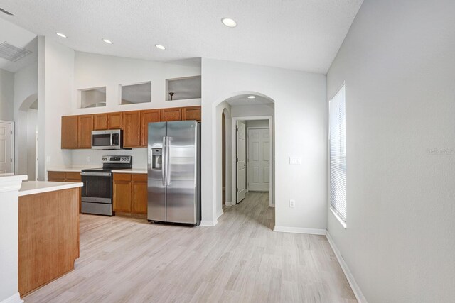 kitchen with a textured ceiling, high vaulted ceiling, light wood-type flooring, and appliances with stainless steel finishes