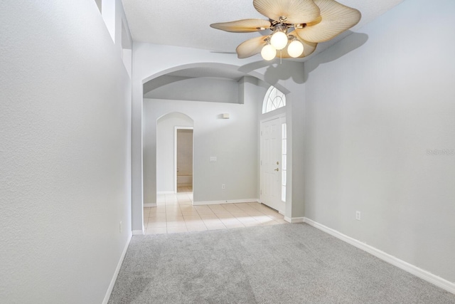 tiled empty room with baseboards, arched walkways, carpet floors, and ceiling fan