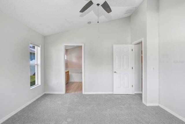 unfurnished bedroom with ensuite bath, vaulted ceiling, light carpet, and ceiling fan