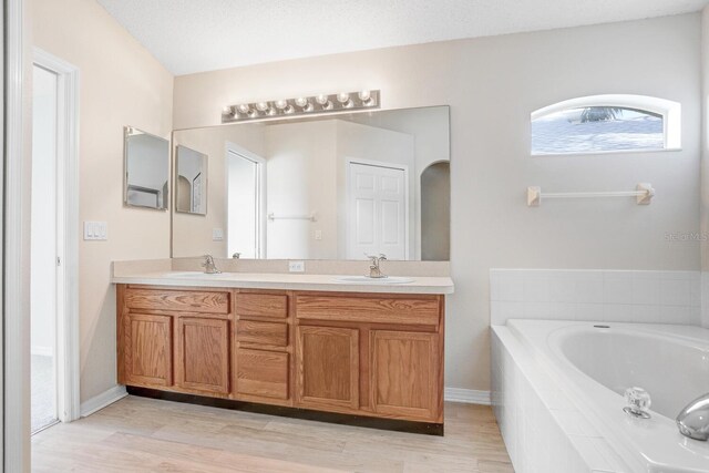 bathroom featuring vanity, a textured ceiling, a relaxing tiled tub, and wood-type flooring