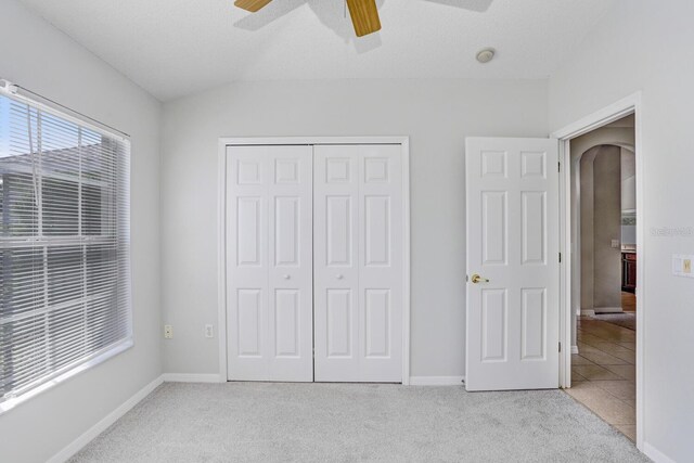 unfurnished bedroom with light colored carpet, ceiling fan, a closet, and vaulted ceiling