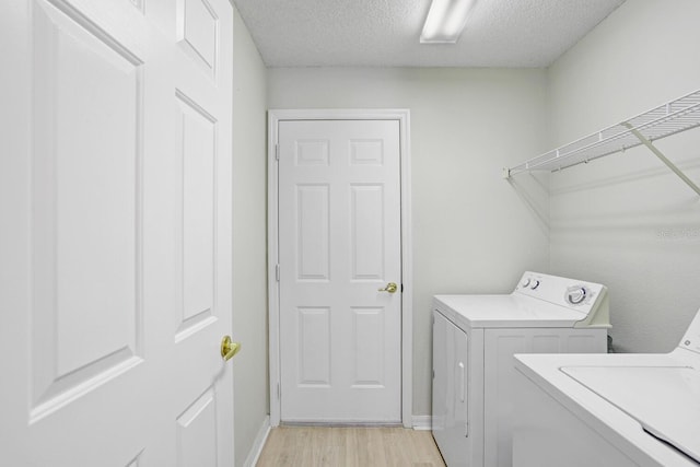 laundry area with independent washer and dryer, a textured ceiling, light wood-style floors, baseboards, and laundry area