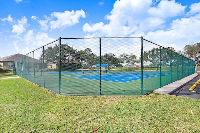 view of tennis court with a lawn and fence