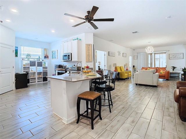 kitchen featuring a breakfast bar, sink, a center island with sink, appliances with stainless steel finishes, and white cabinets