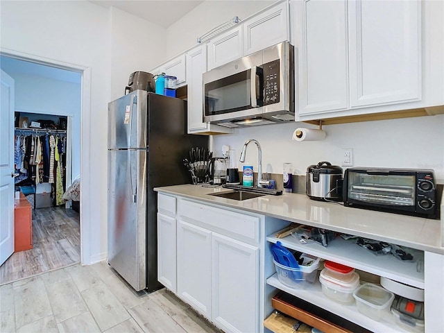 kitchen with appliances with stainless steel finishes, sink, white cabinets, and light wood-type flooring