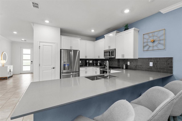 kitchen featuring stainless steel appliances, kitchen peninsula, decorative backsplash, a breakfast bar area, and white cabinets