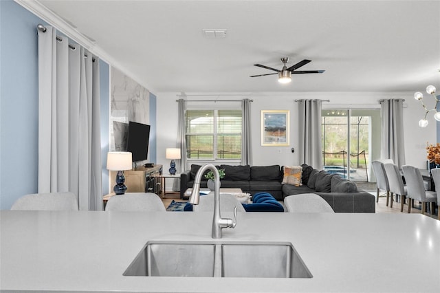 living room featuring ceiling fan with notable chandelier, crown molding, a healthy amount of sunlight, and sink