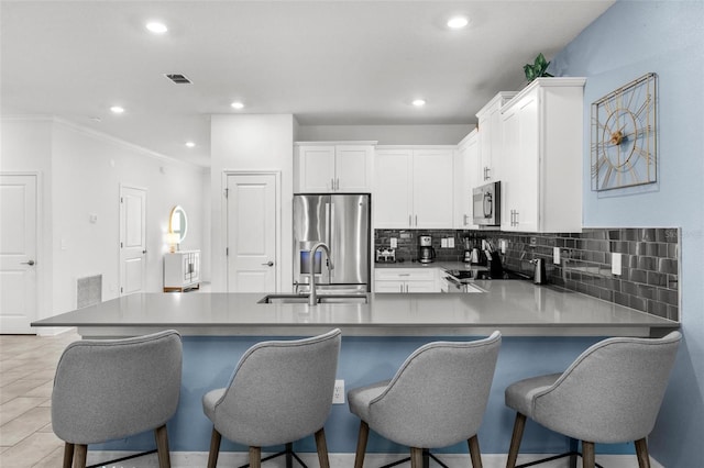 kitchen featuring a breakfast bar area, visible vents, appliances with stainless steel finishes, white cabinets, and a sink