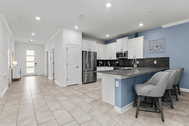 kitchen featuring appliances with stainless steel finishes, a breakfast bar, ornamental molding, a peninsula, and white cabinetry